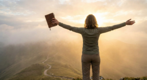 A person standing on a mountain peak at sunrise with arms outstretched, holding a journal and embracing the golden light, symbolizing the journey of manifestation for spiritual growth.