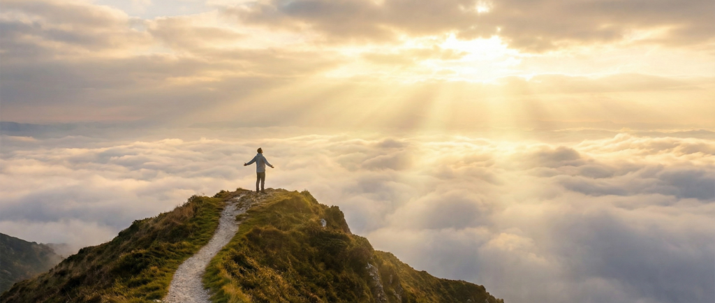 A person standing on a misty mountain peak with arms open to the sunrise, symbolizing the moment of clarity after experiencing confusing spiritual awakening symptoms.