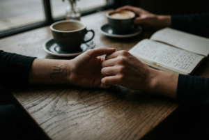 Close-up of two hands holding on a wooden table, one with a Scorpio zodiac constellation tattoo, illustrating zodiac sign attachment styles in relationships.